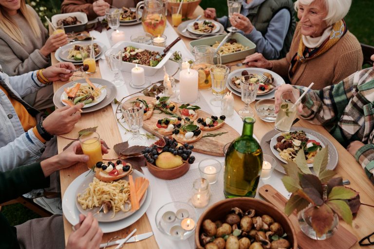 From above crop people enjoying festive dinner with snacks at garden table with candles burning